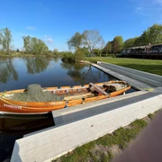 Ein traditionelles Holzboot mit der Aufschrift "Hannover" liegt an einem ruhigen Flussufer vertäut.