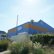 Verwell Verden Wellnessbad mit markant blauer und oranger Fassade, umgeben von blühenden Gräsern bei klarem Himmel.