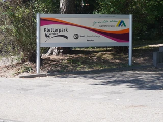 Kletterpark Verden Schild am Eingang des Kletterparks Verden, umgeben von Bäumen und Wegen.
