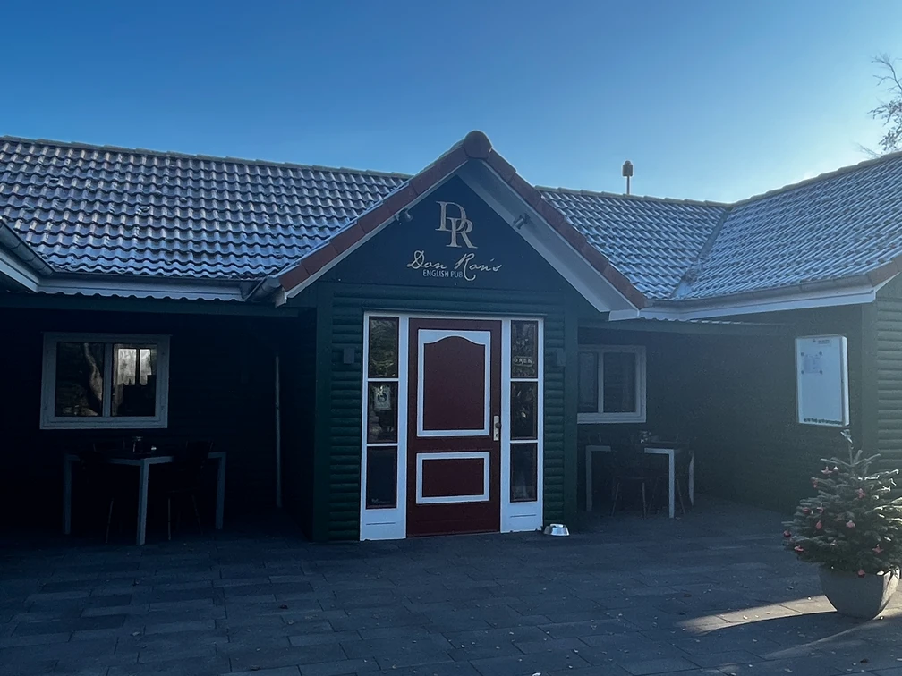 Gemütliches englisches Pub mit dunkelgrüner Fassade und roten Akzenten, umgeben von klarer Natur.