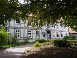Museum Domherrenhaus Ein zweigeschossiges Fachwerkhaus mit weißen Wänden, umgeben von Bäumen und einem Weg im Vordergrund.