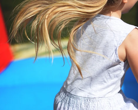 Kinderfest Junge Mädchen mit flatternden Haaren im weißen Kleid beim fröhlichen Spielen vor buntem Hintergrund.Young girl with fluttering hair in a white dress playing happily in front of a colorful background.Jong meisje met wapperend haar in een witte jurk speelt vrolijk voor een kleurrijke achtergrond.