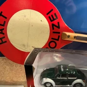 Ein altes Polizeischild mit einem Miniaturmodell eines grünen VW Käfer Polizeiautos im Vordergrund.
