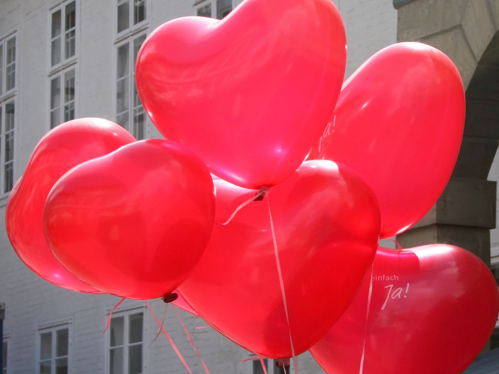 Rote Herzballons schweben vor weißen Backsteinwänden, sorgen für eine fröhliche, festliche Stimmung.