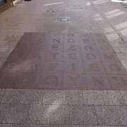 Bodenfliesen Bodenfliesen mit eingravierten Buchstaben und Wörtern, von Sonnenlicht und Schatten bedeckt.