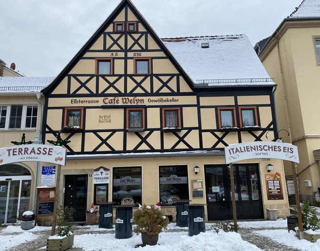 Café Welyn Fachwerkhaus mit Café und Eisdiele, beschneit, mit Schildern "Terrasse" und "Italienisches Eis", umgeben von winterlicher Atmosphäre.