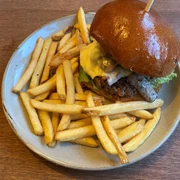 Ein saftiger Burger mit geschmolzenem Käse und goldbraunen Pommes Frites auf einem Keramikteller.