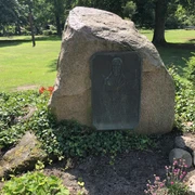 Gedenkstein Hoppe Gedenkstein aus Naturstein mit Gedenktafel in einem gepflegten Park, umgeben von blühenden Pflanzen.