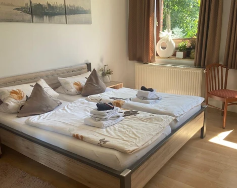 Gästehaus Sorban.jpg Einladendes Gästezimmer mit Doppelbett, natürlichem Licht, geschmackvoller Deko und Holzboden.