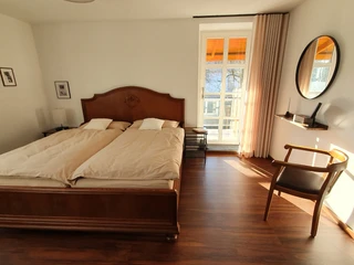 Helles Gästezimmer mit einem Kingsize-Holzbett, schlichter Dekoration und einem Fenster mit Blick ins Freie.