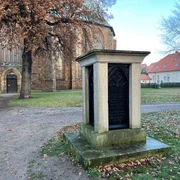 Bischofsdenkmal Verden Ein steinernes Monument gewidmet einem Bischof vor der Kulisse einer historischen Backsteinkirche.