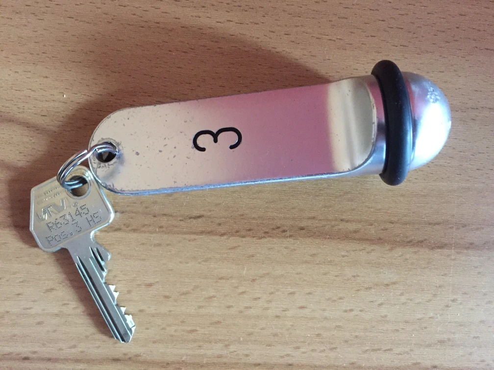 Hotel-Schlüssel Ein Metallschlüsselanhänger mit der Nummer 3 und einem daran befestigten Schlüssel auf Holzoberfläche.