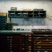 Druckerbande Graue Wand mit etlichen Regalen mit Schubladen davor, Werkstadttcharakter