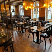 NieheimRestaurantDakos.jpg Restaurant mit dunklen Holzmöbeln, warmen Beleuchtung und Backsteinwänden, einladender Innenraum.