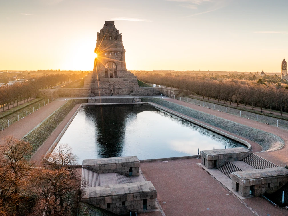 Völkerschlachtdenkmal beim Sonnenaufgang - Kultur in Leipzig Blick auf das Völkerschlachtdenkmal, den See der Tränen und das Krematorium des Südfriedhofes, während die Sonne hinter dem Denkmal aufgeht, Kultur, Denkmal, Geschichte, Panorama