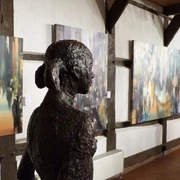 Kunstscheune Steinhude Eine Skulptur aus dunklem Metall steht in einer Galerie, umgeben von farbenfrohen Gemälden.