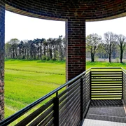 Landschaftsfenster Wemkendorf.JPG Blick durch einen Ziegelbogen auf grüne Wiesen und Bäume. Holzgeländer im Vordergrund.
