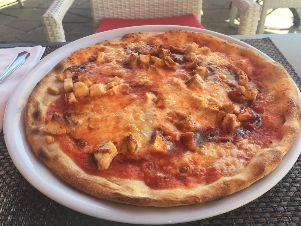 Pizza auf einem weißen Teller, belegt mit saftigen Hühnchenstücken und geschmolzenem Käse.