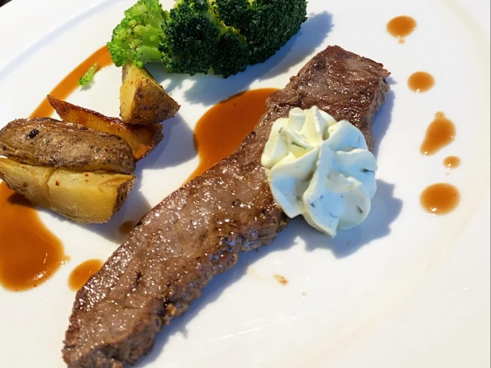 Fleischgericht Saftiges Steak mit Kartoffelspalten, Brokkoli und einer feinen Kräuterbutter auf elegantem Teller.