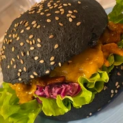 Burger schwarz_CCBYSA_Teutoburger Wald_Stadt Schloss Holte-Stukenbrock-13.jpg Schwarzer Burger mit Sesam, gefüllt mit Salat, rotem Kraut, Käse und gegrilltem Hähnchen auf Teller.
