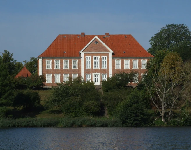 Kreismuseum Herzogtum Lauenburg.JPG Blick vom Ufer auf das Kreismuseum: rotes Gebäude mit weißen Fenstern, davor Wasser und Uferbereich mit Grün