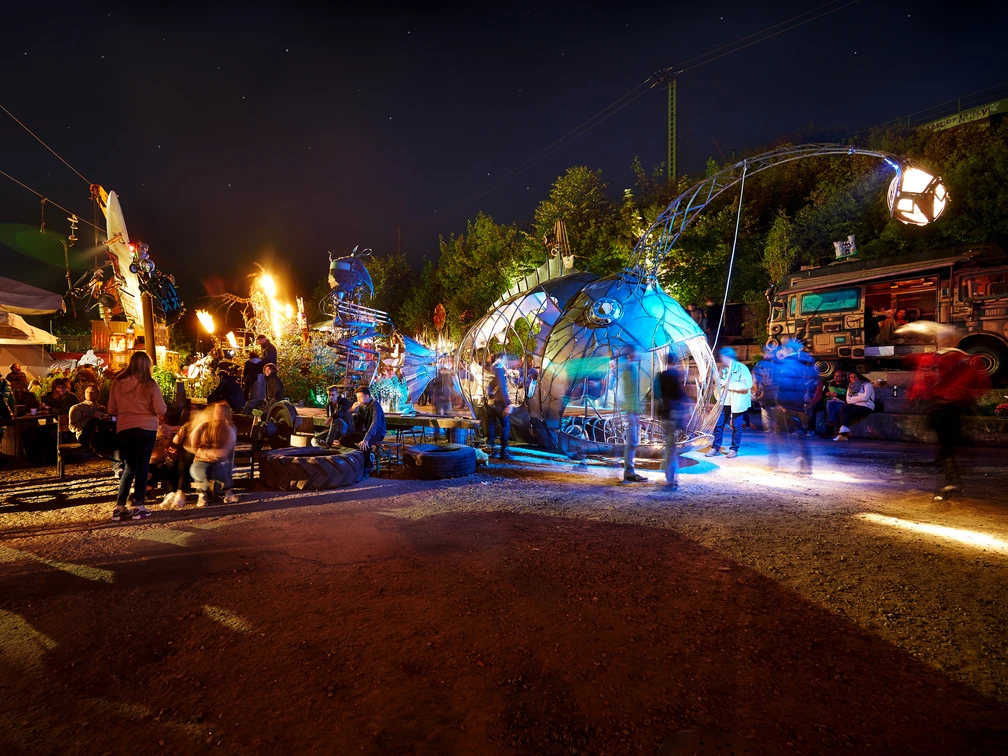 Odonien Nachtszene im Odonien in Köln: Fantasievolle Skulpturen aus Metall und bunte Lichter im Freien.Night scene at Odonien in Cologne: imaginative metal sculptures and colorful outdoor lights.