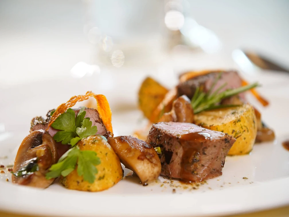 Fein angerichtete Speisen mit Kartoffeln, saftigem Fleisch und Kräutern auf einem weißen Teller.