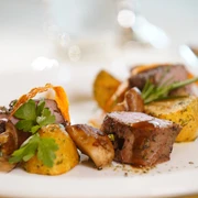 Fein angerichtete Speisen mit Kartoffeln, saftigem Fleisch und Kräutern auf einem weißen Teller.