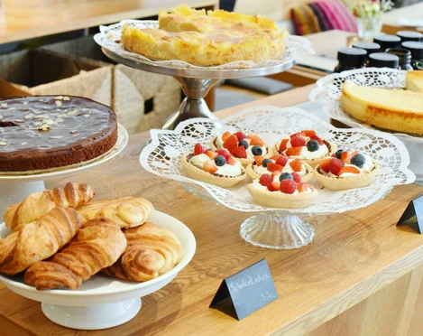 Verschiedene Kuchen und Croissants auf Holztheke, präsentiert auf dekorativen Tortenständern im Café.
