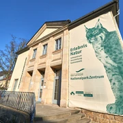 Nationalparkzentrum in Bad Schandau  Eingangsbereich eines Gebäudes mit großem Plakat eines Luchses, das für das Nationalparkzentrum wirbt; blauer Himmel im Hintergrund.