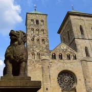 Der sagenhafte Löwenpudel vor dem Osnabrücker Dom Löwenpudel-Skulptur aus Stein mit zwei Türmen des Osnabrücker Doms und blauem Himmel im Hintergrund.Stone sculpture of a lion poodle with two towers of Osnabrück Cathedral and a blue sky in the background.Stenen sculptuur van een leeuwenpoedel met twee torens van de kathedraal van Osnabrück en een blauwe lucht op de achtergrond.