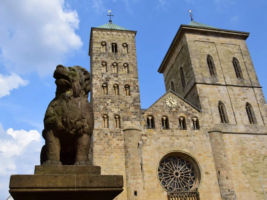 The legendary Löwenpudel in front of St Peter's Cathedral Löwenpudel-Skulptur aus Stein mit zwei Türmen des Osnabrücker Doms und blauem Himmel im Hintergrund.Stone sculpture of a lion poodle with two towers of Osnabrück Cathedral and a blue sky in the background.Stenen sculptuur van een leeuwenpoedel met twee torens van de kathedraal van Osnabrück en een blauwe lucht op de achtergrond.