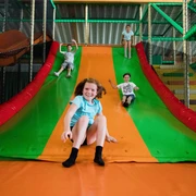 Rutsche im Solivital Sebnitz Vier Kinder rutschen lachend eine große, bunte Rutsche in einem Indoor-Spielplatz hinunter. Die Farben der Rutsche sind grün und orange.