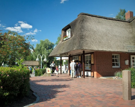 Blick auf Pelz vom Lüneburger Damm.jpg Blick auf eine Eisdiele in einem Reetdachhaus, vor der Menschen stehen und in einer Schlange auf ihr Eis warten