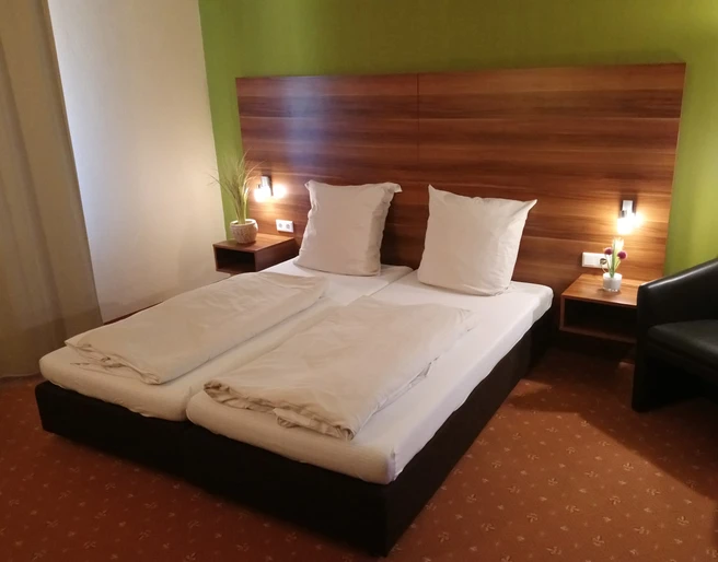 DSC_2314.JPG Ein modernes Doppelzimmer mit grüner Akzentwand, zwei Einzelbetten, Nachttischlampen und einer Sitzgelegenheit.