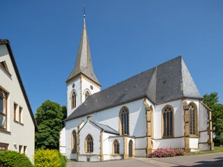Oerlinghausen-Alexanderkirche-Teutoburger-Wald-Tourismus-Patrick-Gawandtka-058 - Kopie-CC-BY-SA.jpg Klassische Kirche mit hohem Turm und Spitzdach, umgeben von grünen Bäumen unter klarem Himmel.