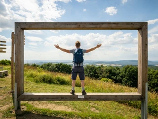 Lügde-Köterberg-Teutoburger-Wald-Tourismus-D-Ketz-069.jpg Mann mit Rucksack steht auf einer Holzplattform, ausgebreitet, mit Blick auf hügelige Landschaft.
