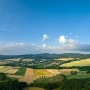 Panoramablick über eine ländliche Region mit Feldern, Wäldern und kleinen Dörfern unter blauem Himmel.