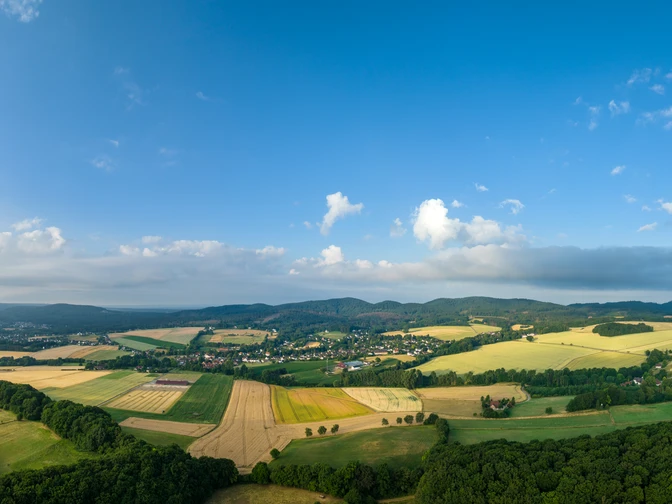 Panoramablick über eine ländliche Region mit Feldern, Wäldern und kleinen Dörfern unter blauem Himmel.
