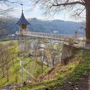 Historischer Personenaufzug Bad Schandau Eine Metallbrücke mit einem kleinen Turm führt über eine grüne Landschaft mit Bäumen und Hügeln im Hintergrund, bei sonnigem Wetter.