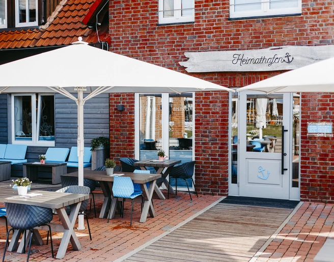 Heimathafen Außenbereich eines Restaurants im maritimen Stil mit Holztischen, blauen Stühlen und Sonnenschirmen.