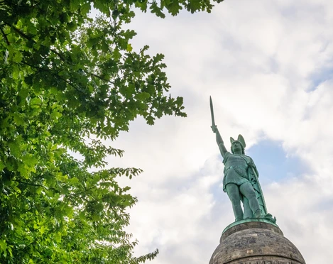 Detmold-Hermannsdenkmal-Teutoburger-Wald-Tourismus-D-Ketz-004-CC-BY-SA.jpg Hermannsdenkmal in Detmold vor bewölktem Himmel, von Bäumen eingerahmt, erhobenes Schwert.