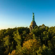 Detmold-Hermannsdenkmal-Teutoburger-Wald-Tourismus-D-Ketz-106.jpg Denkmal auf bewaldetem Hügel bei Sonnenuntergang, im Hintergrund blauer Himmel.