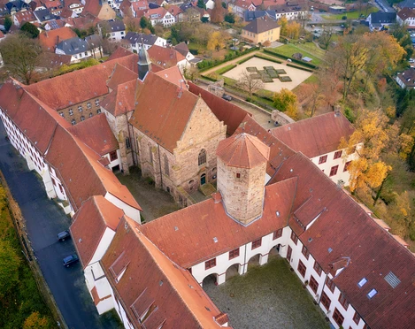 Luftaufnahme eines historischen Klosterkomplexes mit roten Ziegeldächern und Herbstbäumen.