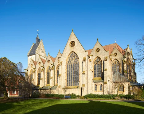 Gotische Kirche aus Sandstein mit großen Buntglasfenstern und gepflegtem Rasen im Vordergrund.