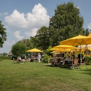 Schirmbar (Jens Butz).jpg Mehrere Personen sitzen unter Sonnenschirmen auf einer Wiese und genießen das schöne Wetter