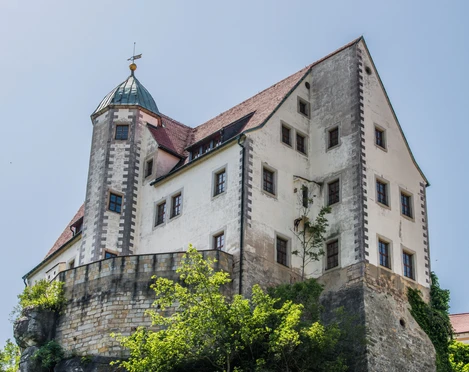 Hohnstein Castle Historisches Schloss mit weißer Fassade und rotem Ziegeldach auf einem Felsen, umgeben von grünen Bäumen, unter klarem, blauem Himmel.