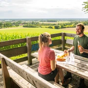 Borgholzhausen-Aussichtsplattform Berghauser Weg-Teutoburger-Wald-Tourismus-D-Ketz-073.jpg Zwei Personen genießen ein Picknick mit Blick auf weite Felder und Wälder von einer Holzplattform.