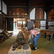Bielefeld-Bauernhausmuseum-Teutoburger-Wald-Tourismus-T-Evers-044.jpg Zwei Personen erkunden ein historisches Bauernhausmuseum, umgeben von alten Küchenutensilien.