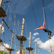 Bielefeld-Kletterpark-Teutoburger-Wald-Tourismus-D-Ketz-028.jpg Kletterpark mit hängender Person in Sicherheitsausrüstung vor blauem Himmel und Seilparcours.